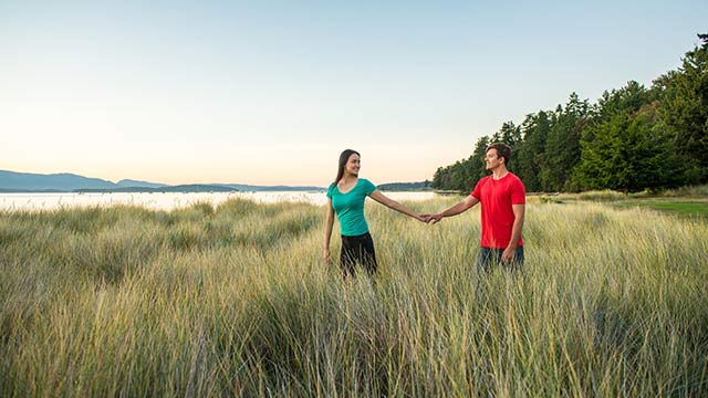  Two adults holding hands on the boardwalk near the water at sunset in Gulf Islands National Park Reserve